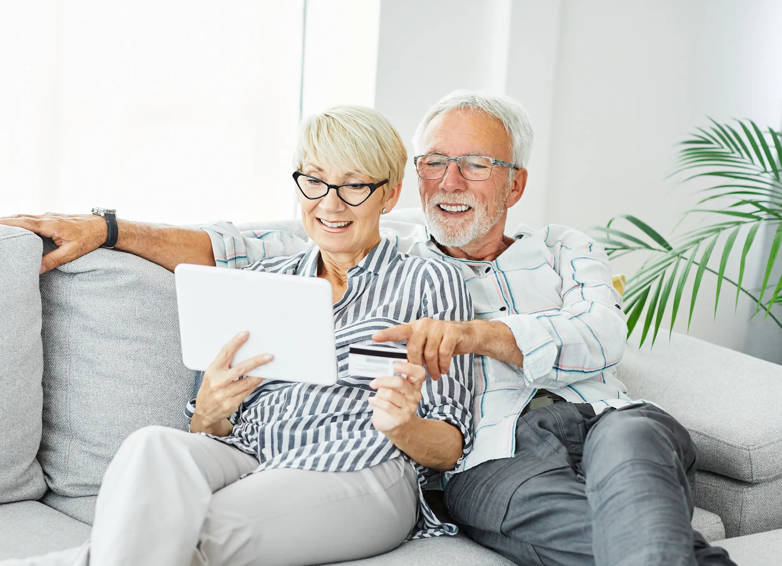 Two residents at The Vista at Sage Hill enjoy online shopping together on a tablet while relaxing on a sofa.